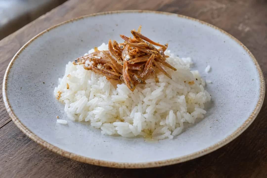 Plated Nasi Lemak with creamy coconut rice, sambal, crispy anchovies, and garnishes.