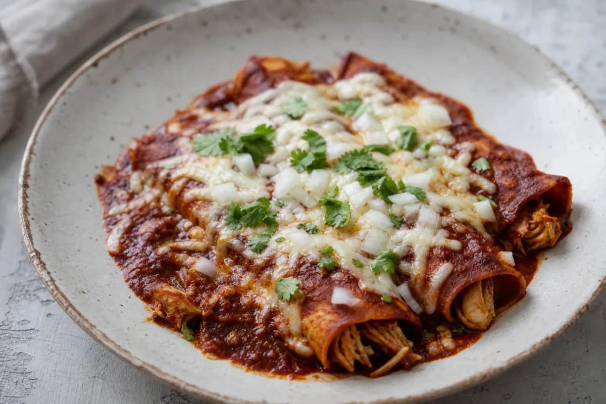 Plated Mexican chicken enchiladas garnished with cheese and cilantro, showcasing vibrant red sauce and soft tortillas.
