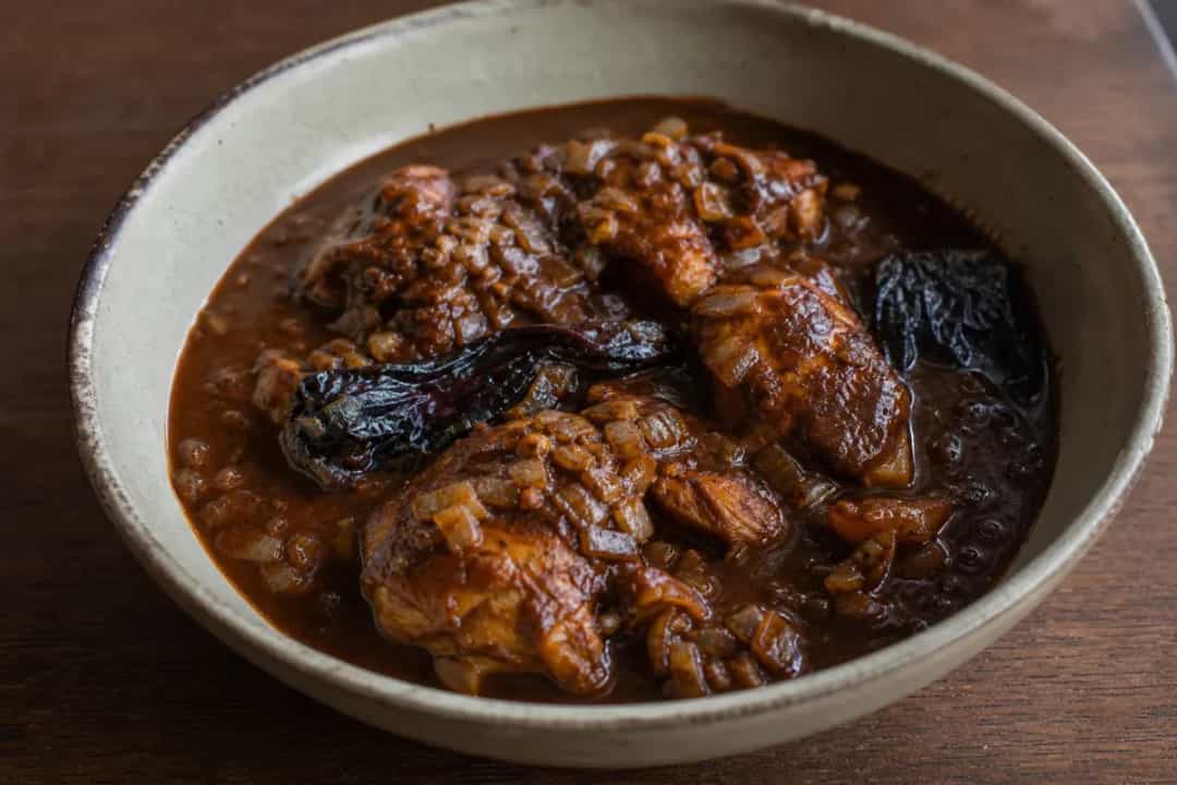 Tender chicken coated in dark, rich mole sauce with chocolate and chilies, garnished with sesame seeds.