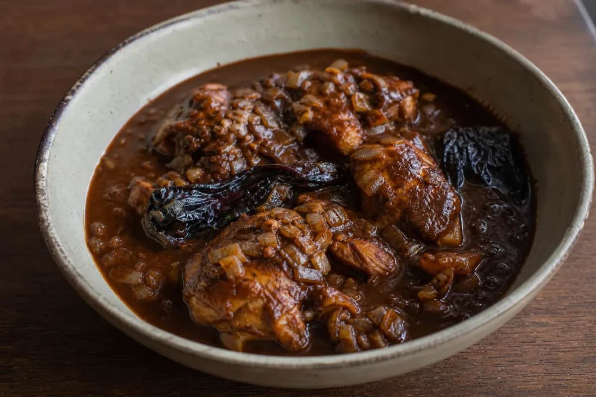 Tender chicken coated in dark, rich mole sauce with chocolate and chilies, garnished with sesame seeds.