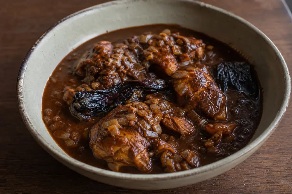 Tender chicken coated in dark, rich mole sauce with chocolate and chilies, garnished with sesame seeds.