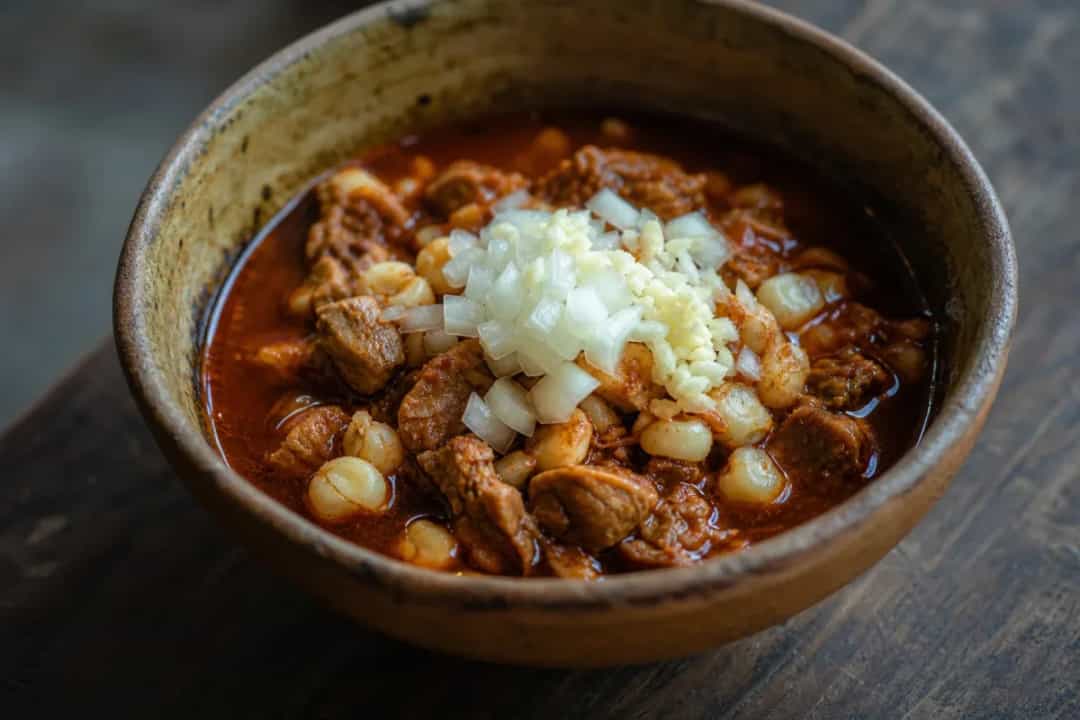 A hearty bowl of pozole rojo garnished with lettuce, radishes, and lime, showcasing tender pork and hominy.