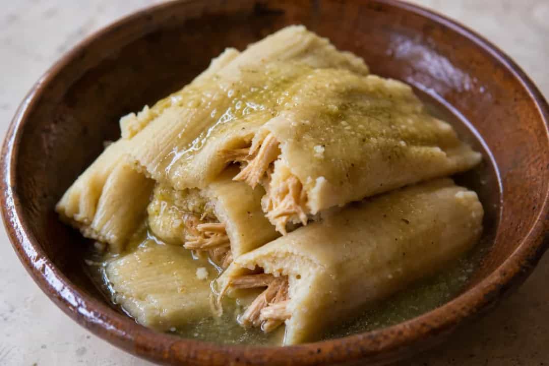 Plated tamales with green salsa, garnished with cilantro and lime, showcasing the texture of masa and chicken filling.