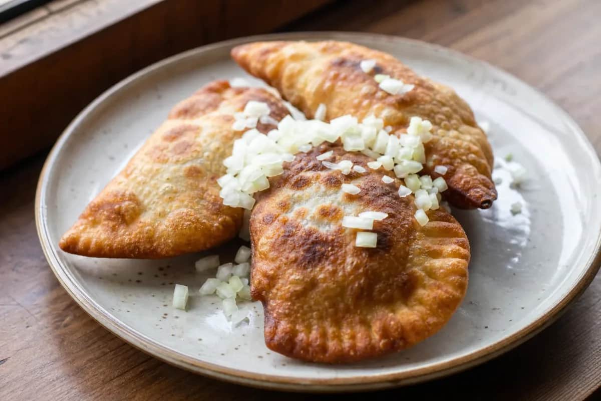 Golden-brown khuushuur with a crispy crust, filled with savory meat, garnished and plated elegantly.