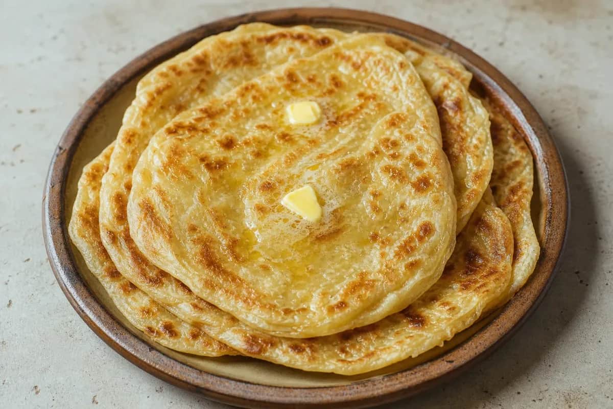 Golden-brown msemen flatbreads stacked on a plate, showcasing flaky layers and a crispy exterior.