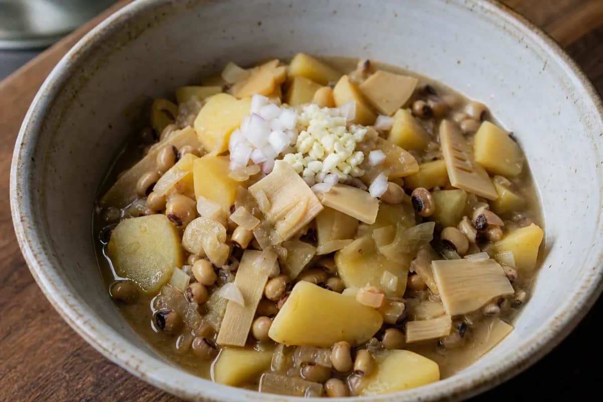 A vibrant bowl of Aloo Tama featuring potatoes, bamboo shoots, and black-eyed peas in a rich curry sauce.