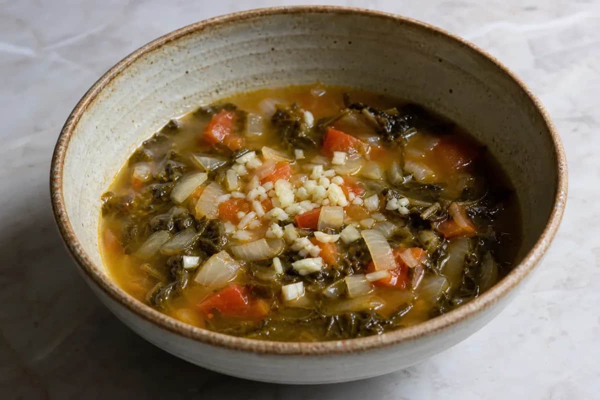 Warm bowl of gundruk soup with vibrant greens, tomatoes, and herbs garnished on top.