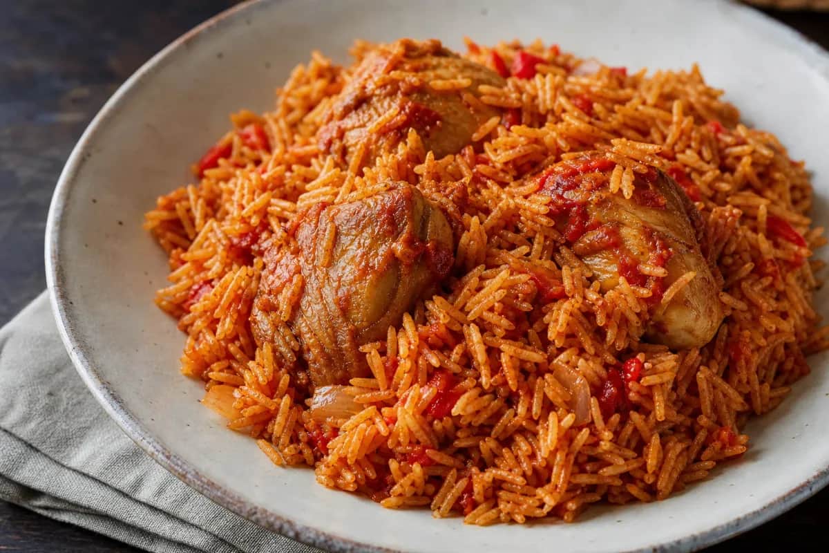 Plated Nigerian Jollof rice with chicken, garnished with fresh vegetables and herbs, showcasing vibrant colors and textures.