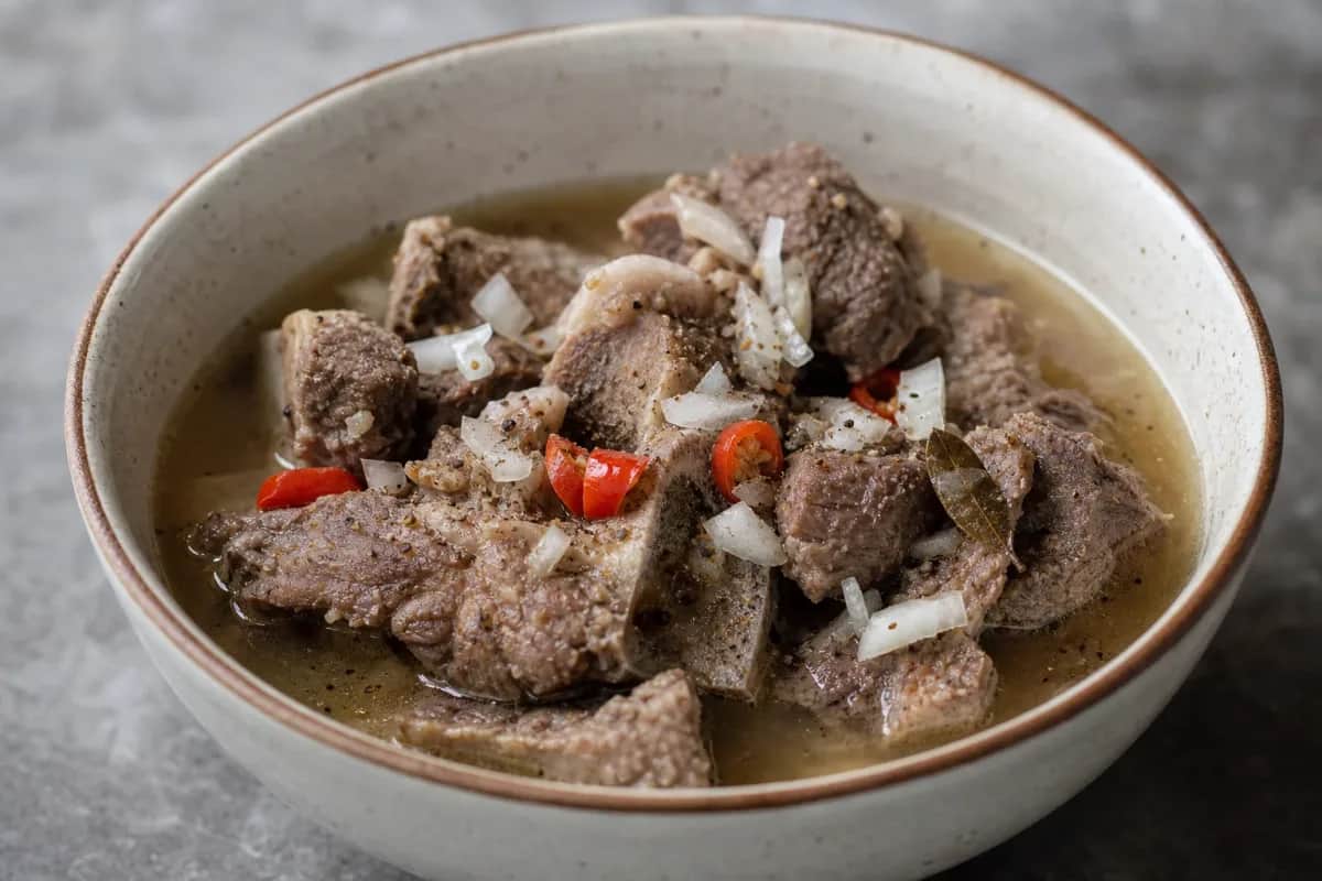 Bowl of Nigerian pepper soup with goat meat, herbs, and spices, garnished with green onions.