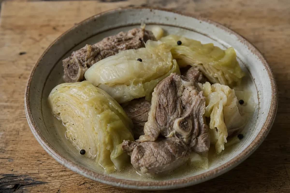 A hearty bowl of fårikål featuring tender lamb pieces and cabbage, garnished with black pepper, showcasing rustic Norwegian cuisine.