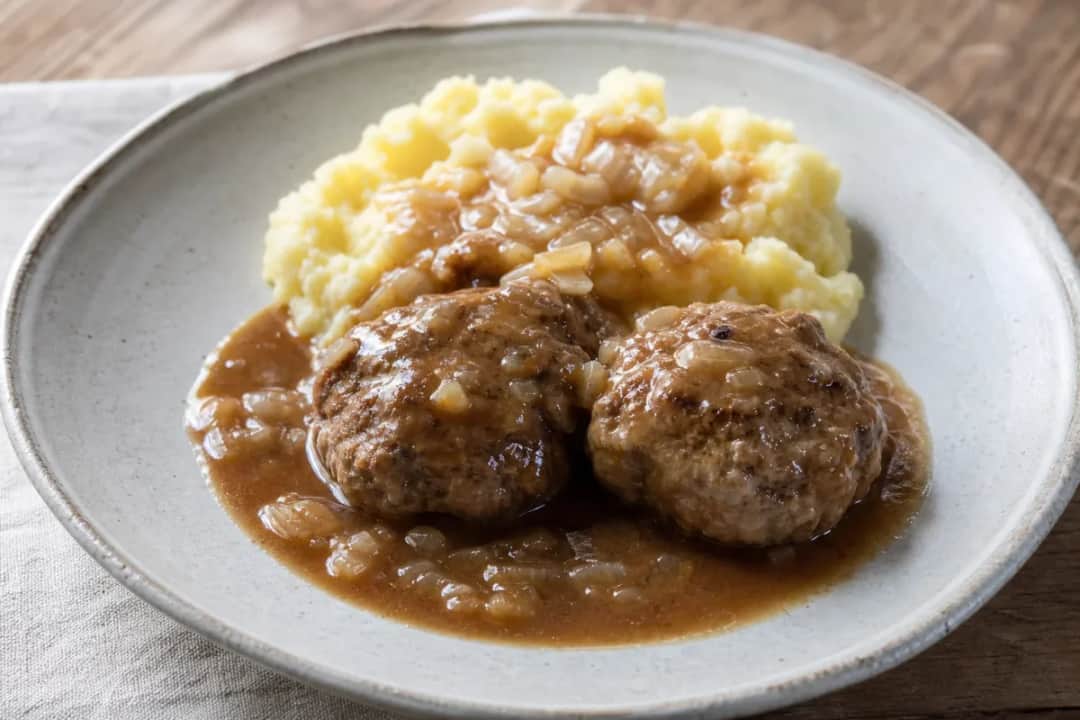 Plated Norwegian kjøttkaker meatballs with brown gravy and smooth mashed potatoes, garnished with parsley.