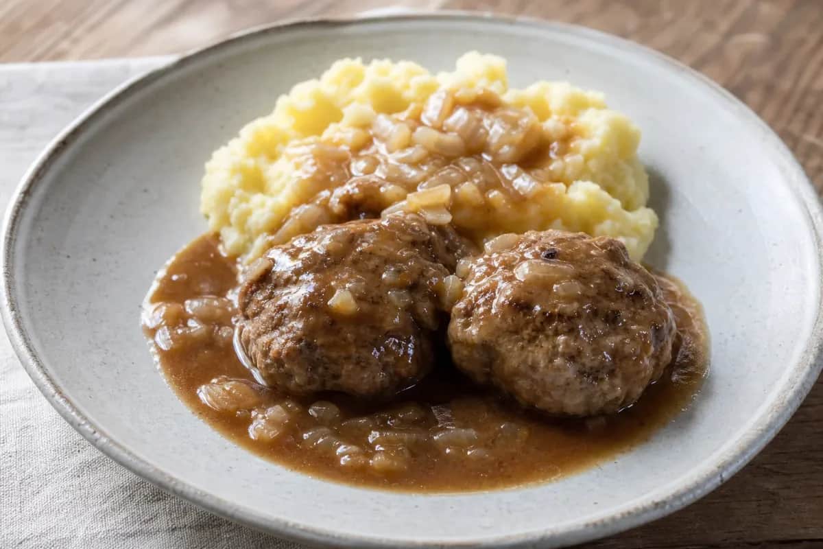 Plated Norwegian kjøttkaker meatballs with brown gravy and smooth mashed potatoes, garnished with parsley.