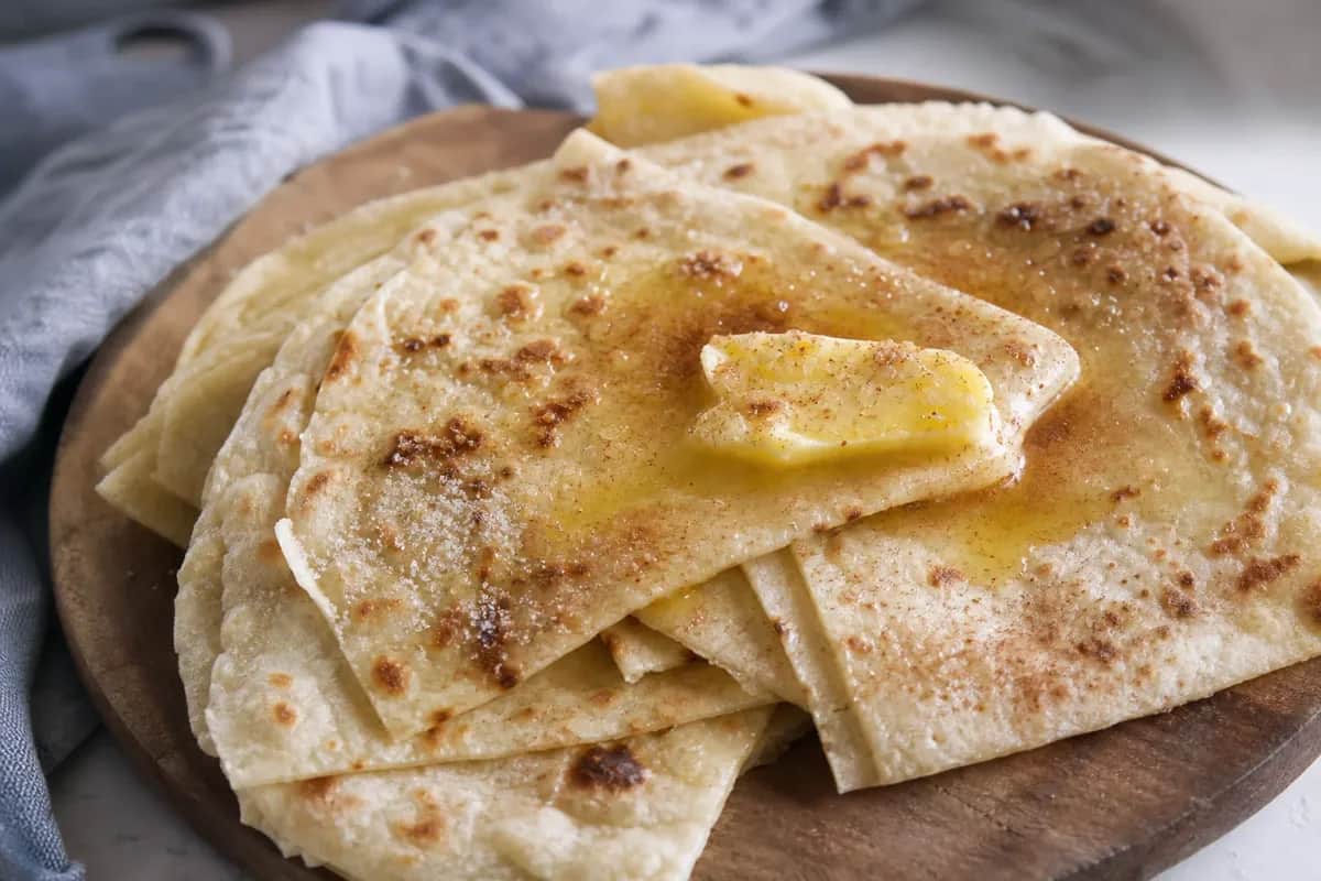 Soft Norwegian lefse topped with melted butter, sugar, and cinnamon, served on a rustic plate.