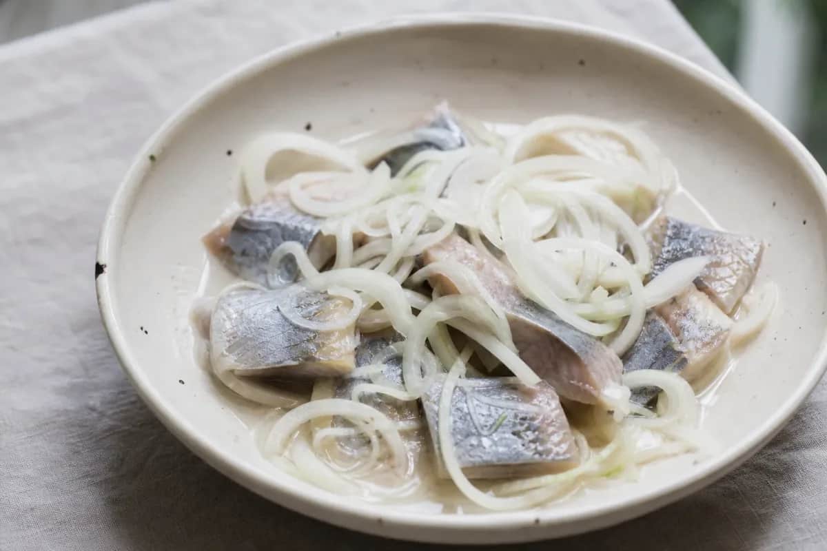 Delicately layered pickled herring garnished with fresh dill and onions, served in a clear dish.