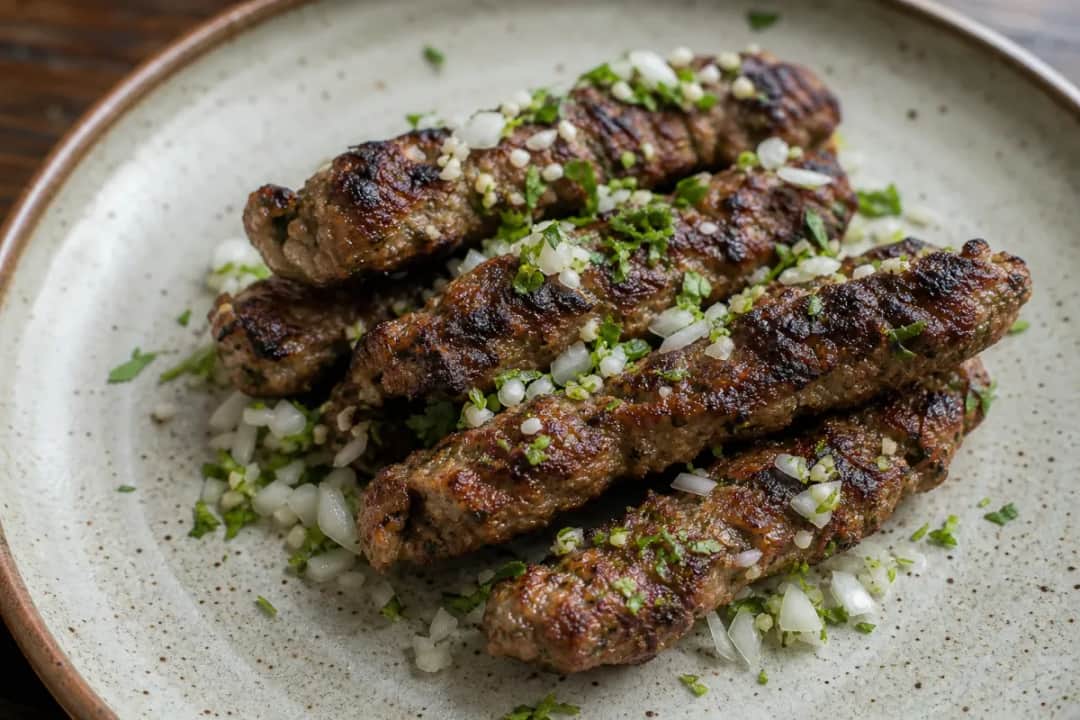 Juicy seekh kebabs with herbs, served on a plate with vibrant green chutney.