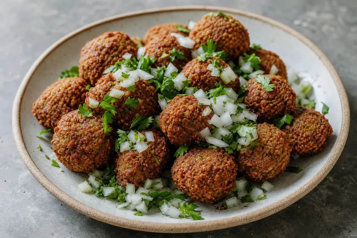 Crispy falafel balls garnished with herbs, served with tahini sauce on a plate.
