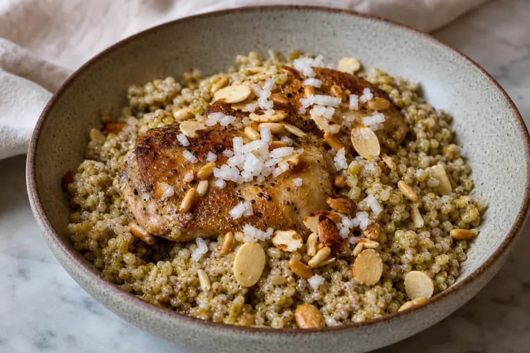 A vibrant plate of freekeh topped with chicken pieces and toasted nuts, garnished with herbs.