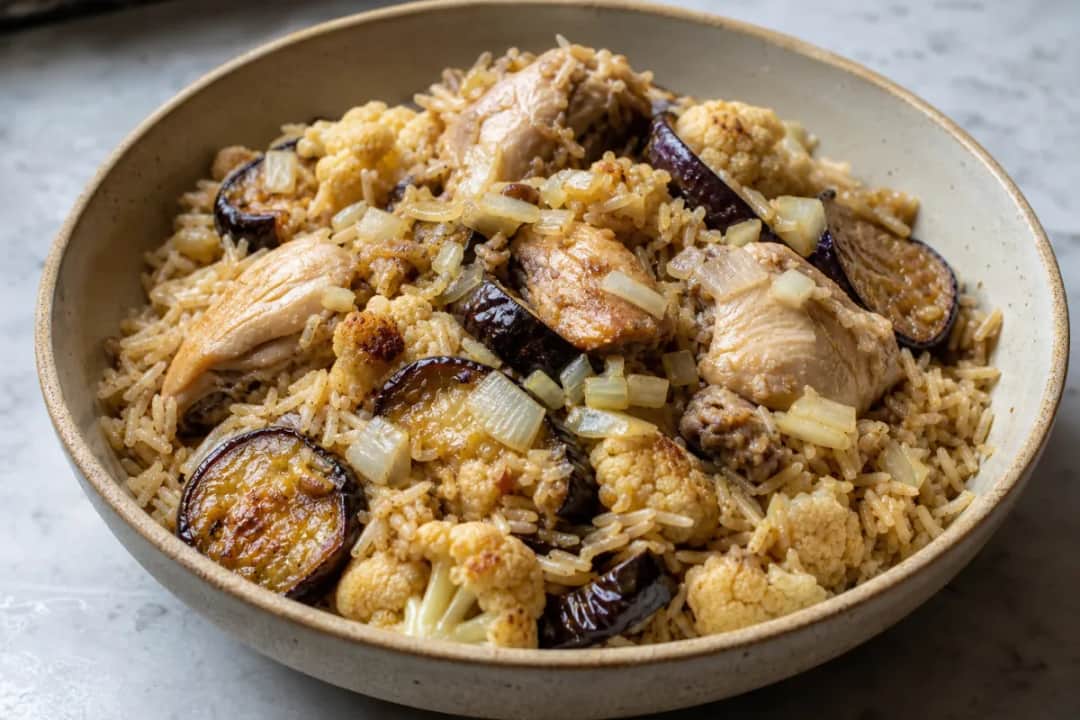 Layered Maqluba featuring chicken, eggplant, and cauliflower with rice, garnished with herbs.