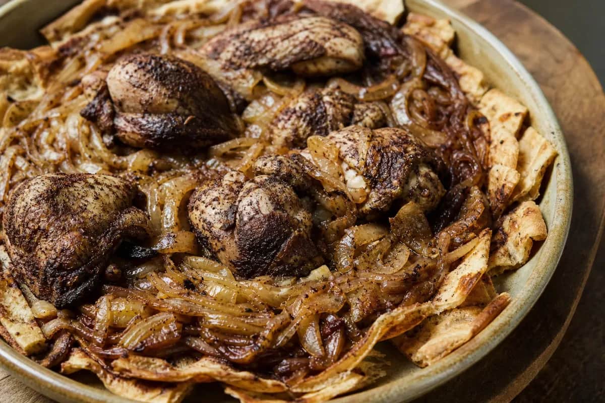 Plated musakhan featuring golden-brown chicken, rich caramelized onions, and flatbread, garnished with pine nuts.