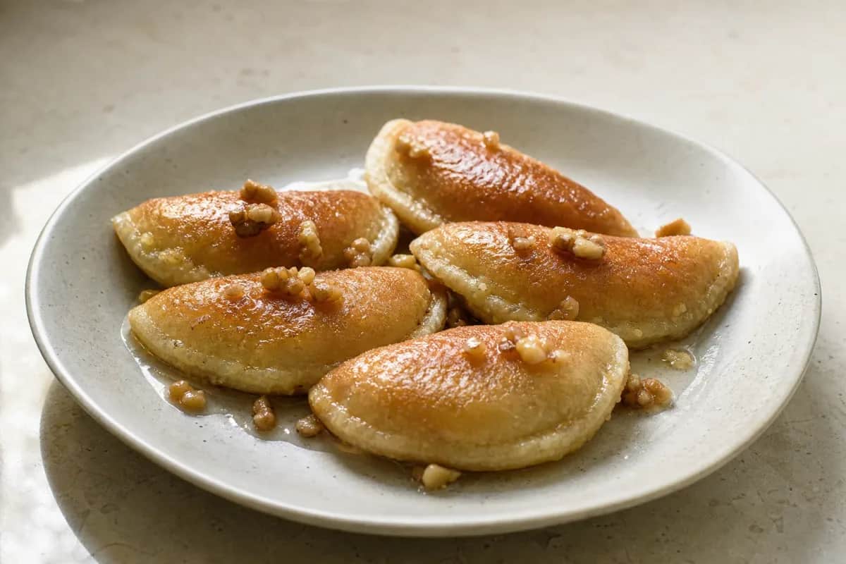 Golden-brown qatayef stuffed with walnuts, drizzled in syrup, plated beautifully.