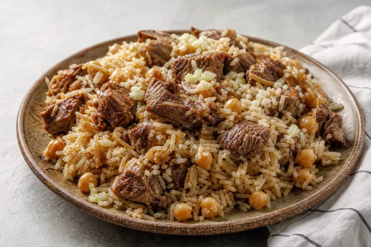 Plated Palestinian Qidreh with tender lamb, chickpeas, and aromatic rice garnished with herbs.