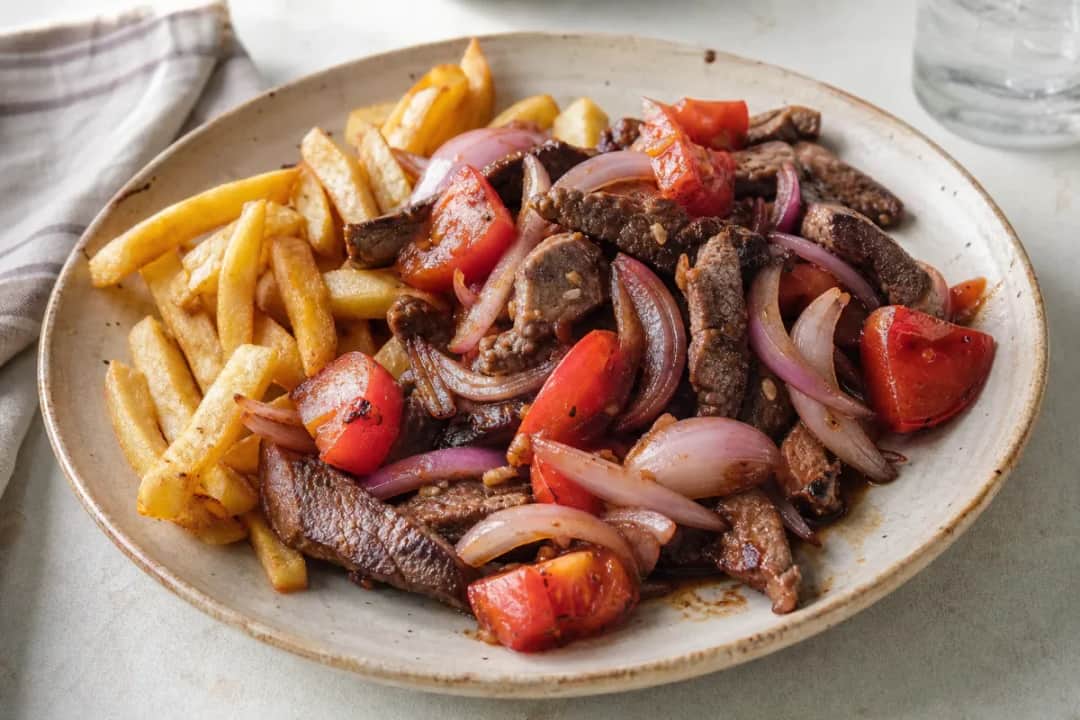 Plated Lomo Saltado with tender beef strips, vibrant tomatoes, and golden crispy fries on a white plate.