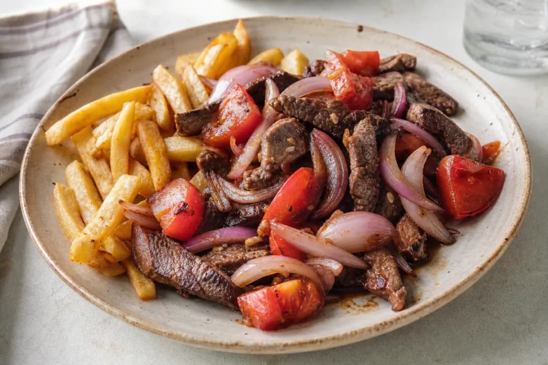 Plated Lomo Saltado with tender beef strips, vibrant tomatoes, and golden crispy fries on a white plate.