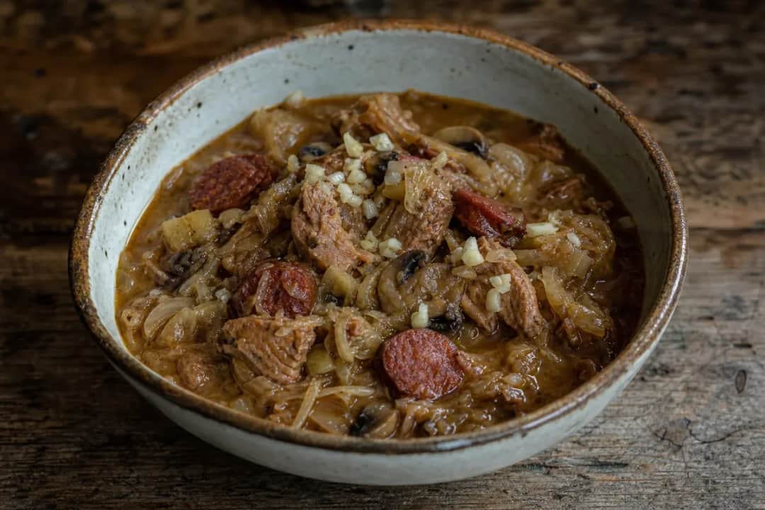 A hearty bowl of bigos stew with sauerkraut, sausage, and meat, garnished with parsley.