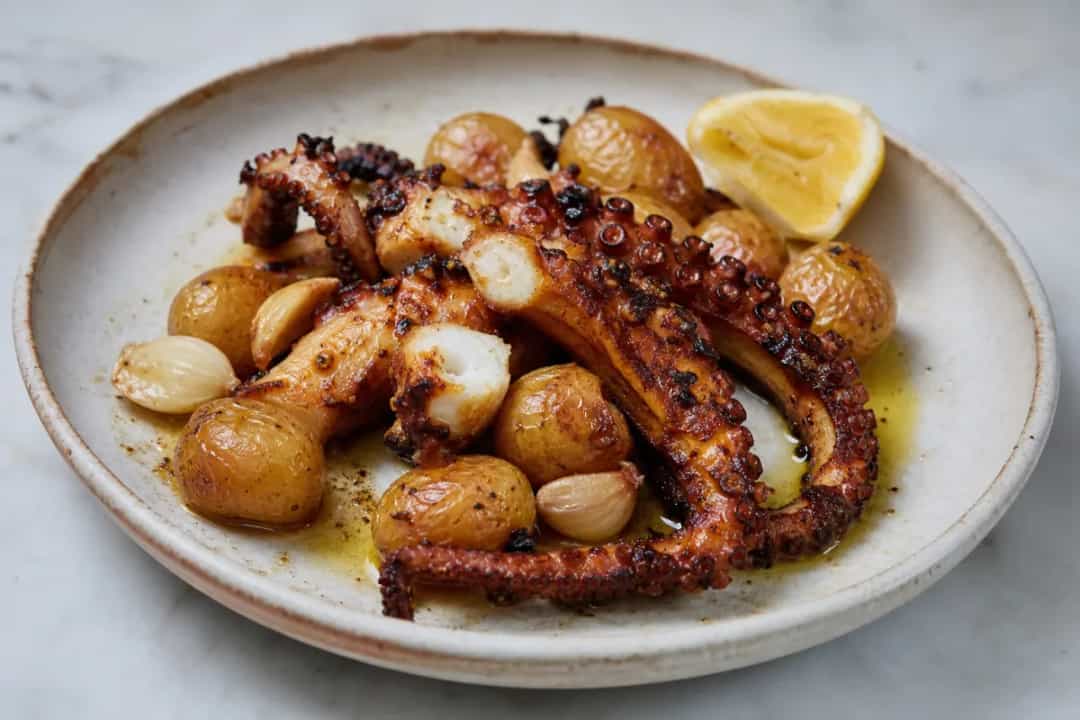 Tender roasted octopus on a plate with golden garlic potatoes and fresh herbs.