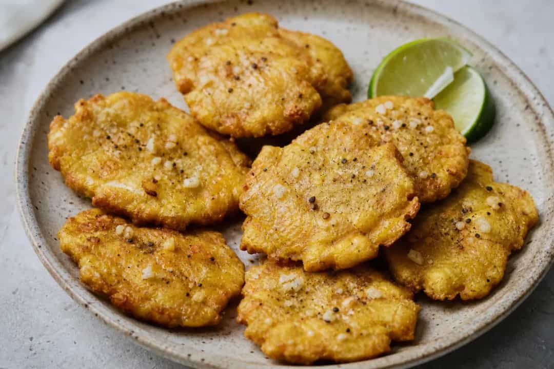 Golden brown tostones served with garlic dipping sauce and fresh herbs, showcasing their crispy texture.
