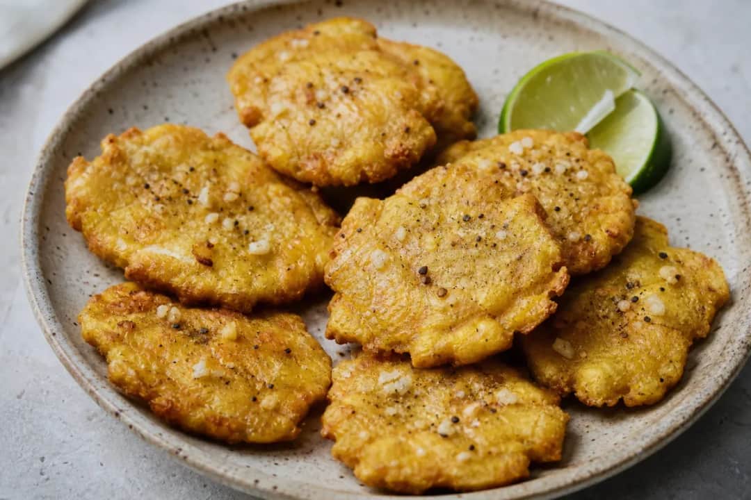 Golden brown tostones served with garlic dipping sauce and fresh herbs, showcasing their crispy texture.
