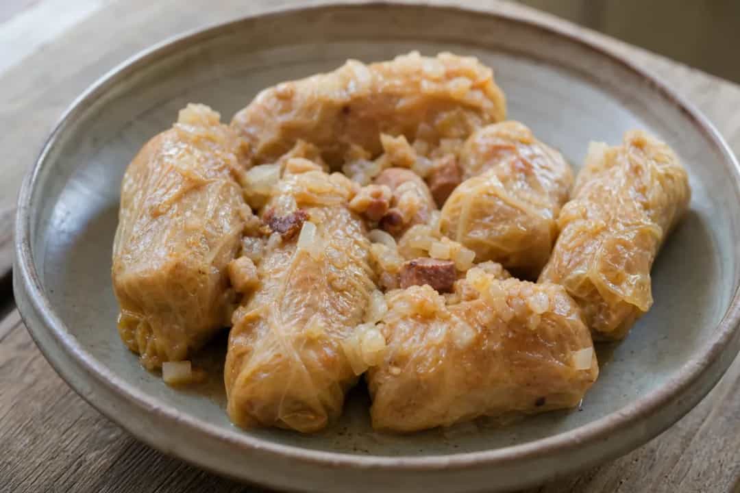 Plated Romanian sarmale with tender cabbage, pork, and rice filling, garnished with herbs.