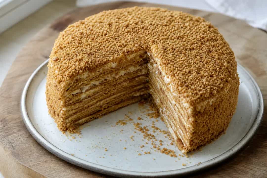 Layered honey cake with creamy filling and crushed nuts on top.