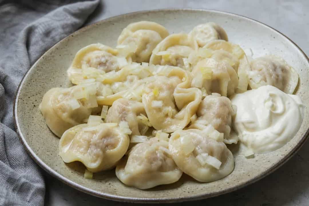 Plated Russian pelmeni dumplings with beef filling, topped with sour cream.