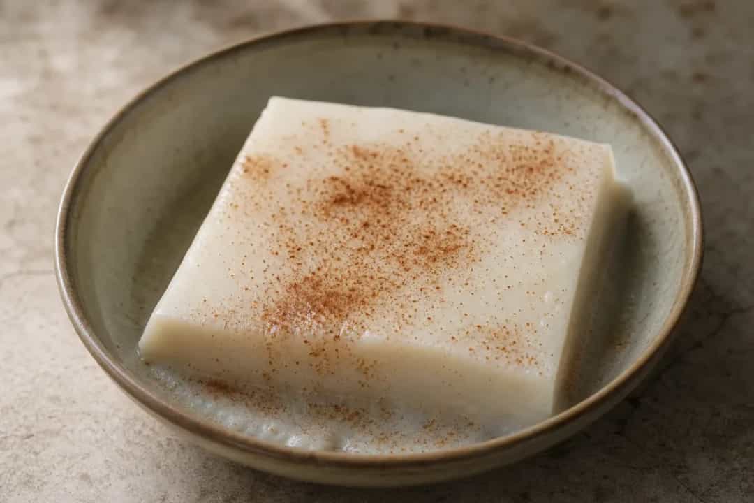Smooth coconut pudding topped with cinnamon, garnished with coconut flakes, served in a decorative dish.