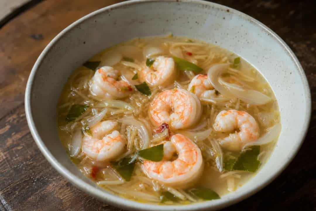 Bowl of Tom Yum Goong with shrimp, herbs, and lime, garnished beautifully.