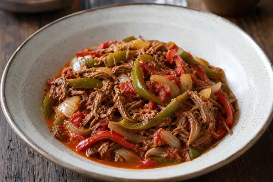 Plated Cuban Ropa Vieja with shredded beef, vibrant bell peppers, and rich tomato sauce served with rice.