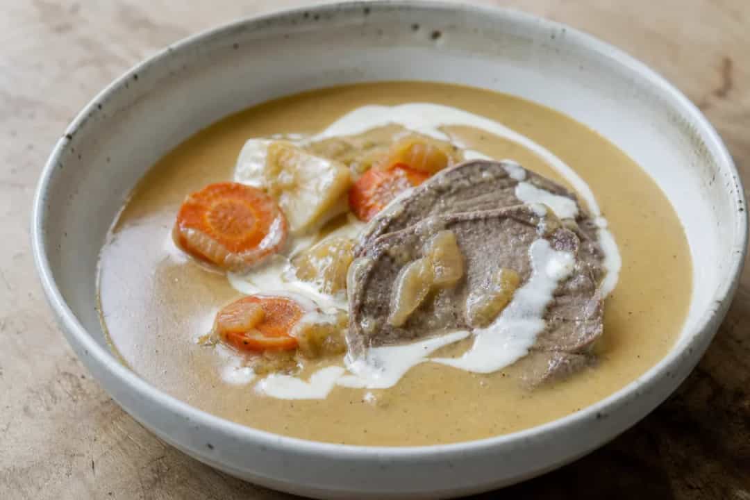 Tender beef sirloin garnished with creamy sauce, served with colorful vegetables on a plate.