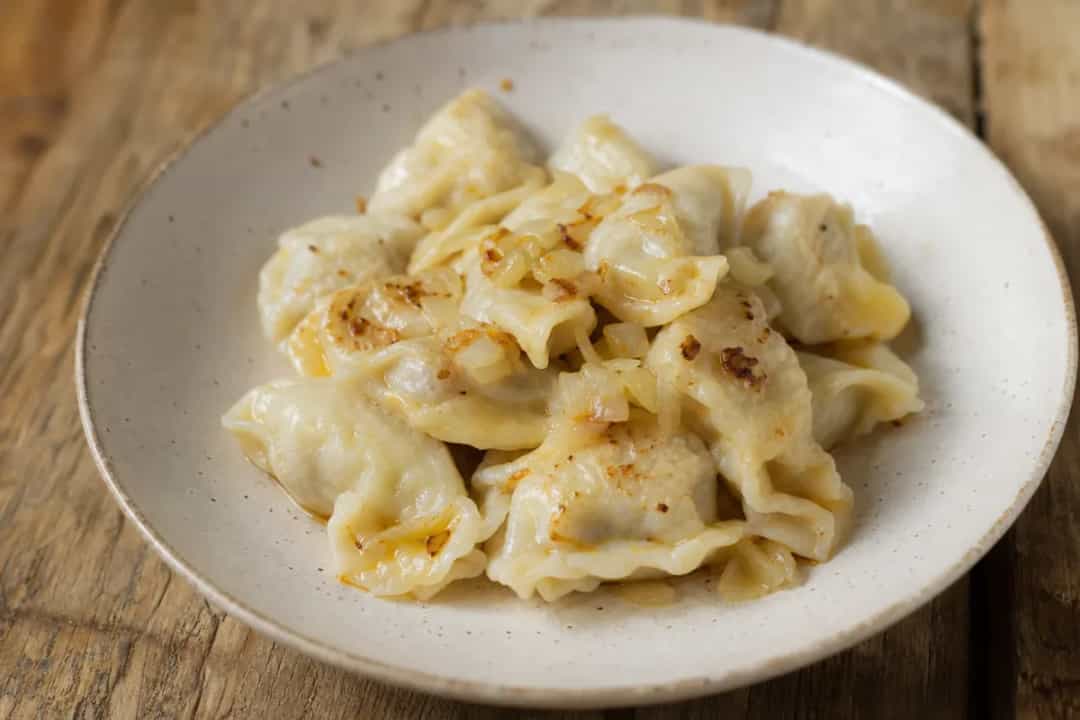 Plated Idrijski Žlikrofi dumplings garnished with herbs, showcasing the soft texture and savory filling.