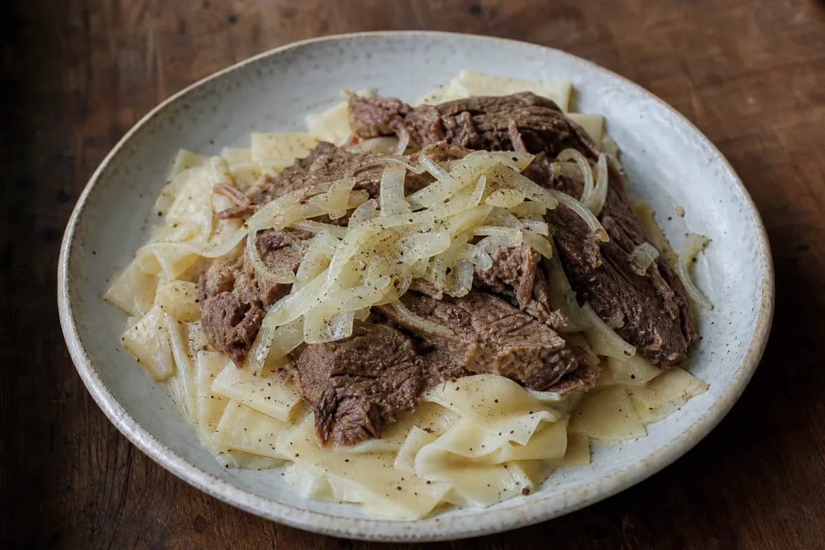 Plated dish of beshbarmak featuring tender beef, handmade noodles, and onions, garnished elegantly.