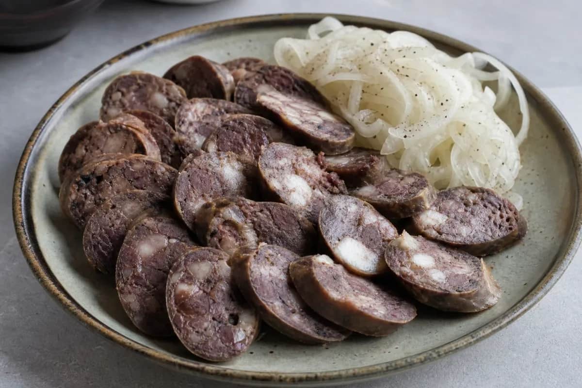 A vibrant platter featuring sliced Kazakh Kazy sausage, garnished with colorful pickled onions and fresh herbs.