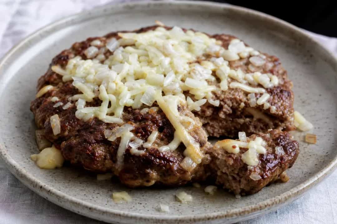 Juicy Serbian pljeskavica burger stuffed with cheese, garnished with fresh vegetables and served on a plate.