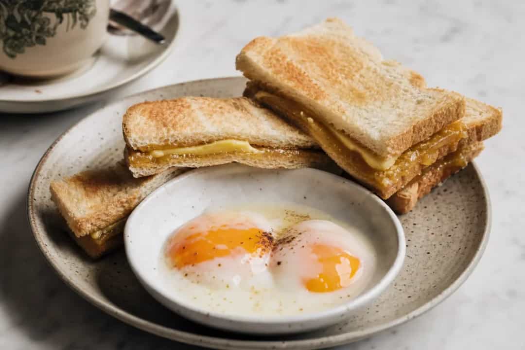 Kaya toast slices with coconut jam, soft-boiled eggs, and a cup of coffee on the side.
