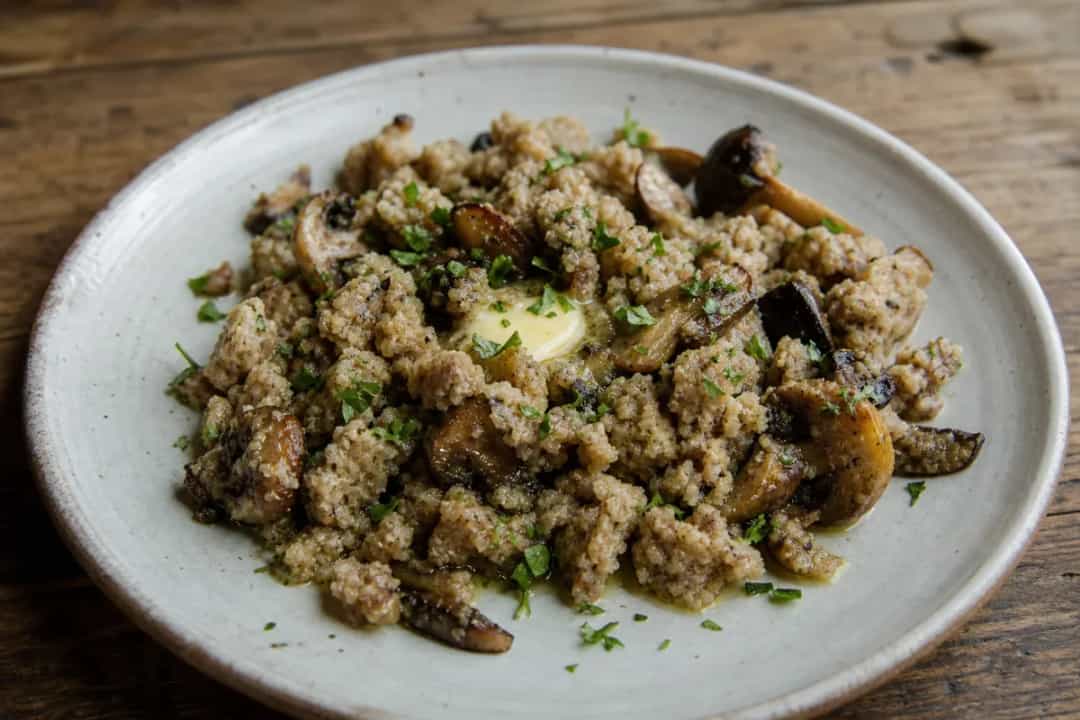 Plated buckwheat žganci topped with sautéed mushrooms and herbs, showcasing a rustic texture.