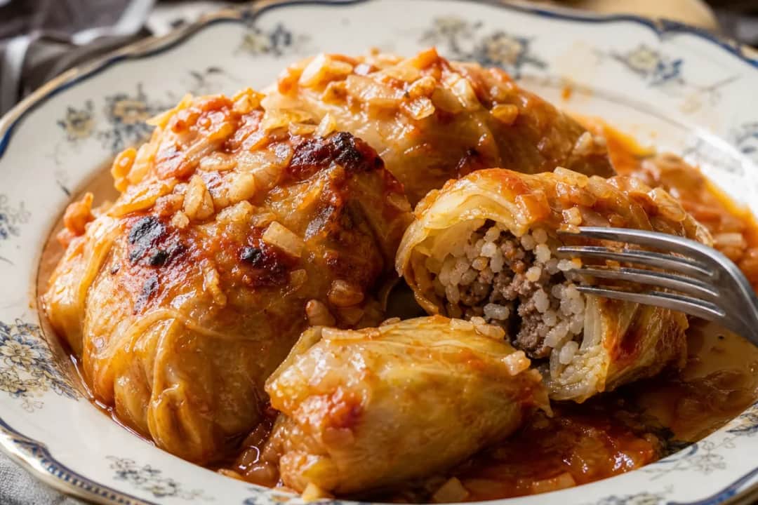 Plated Ukrainian holubtsi with beef and rice filling, topped with tomato sauce.