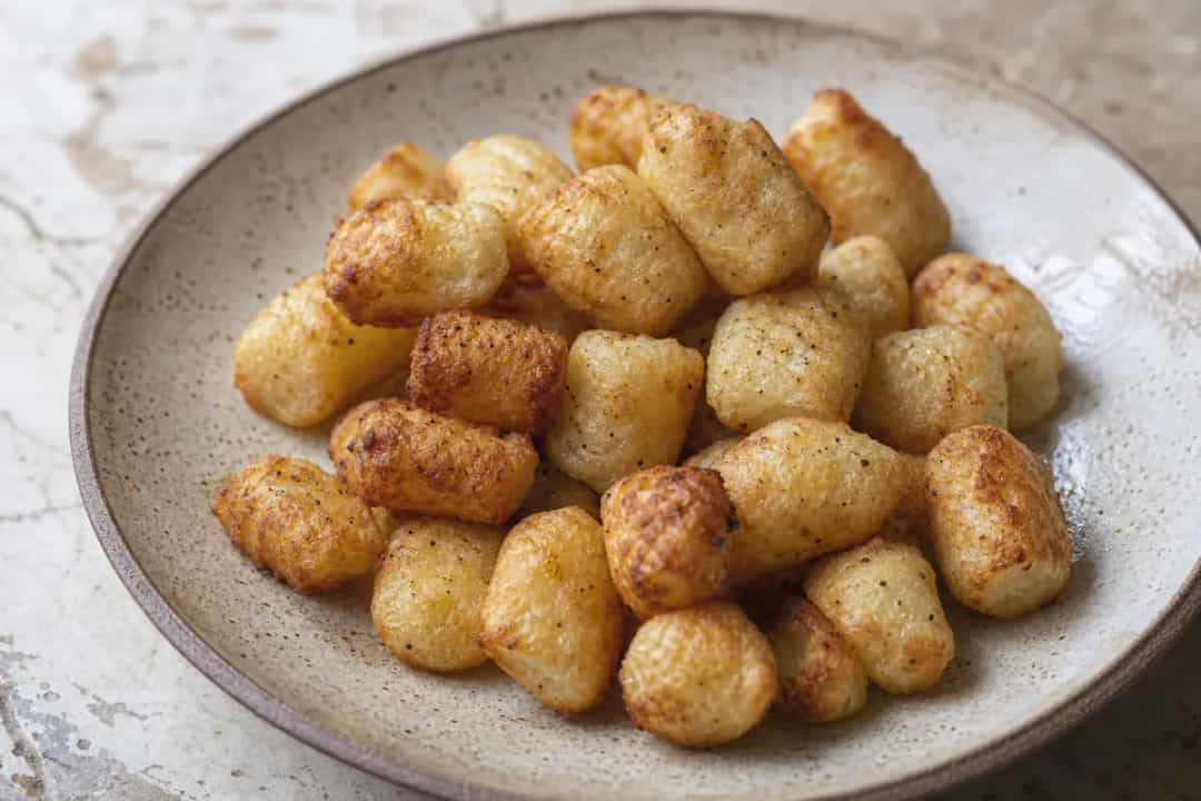 Crispy golden potato pillows topped with herbs, served on a plate