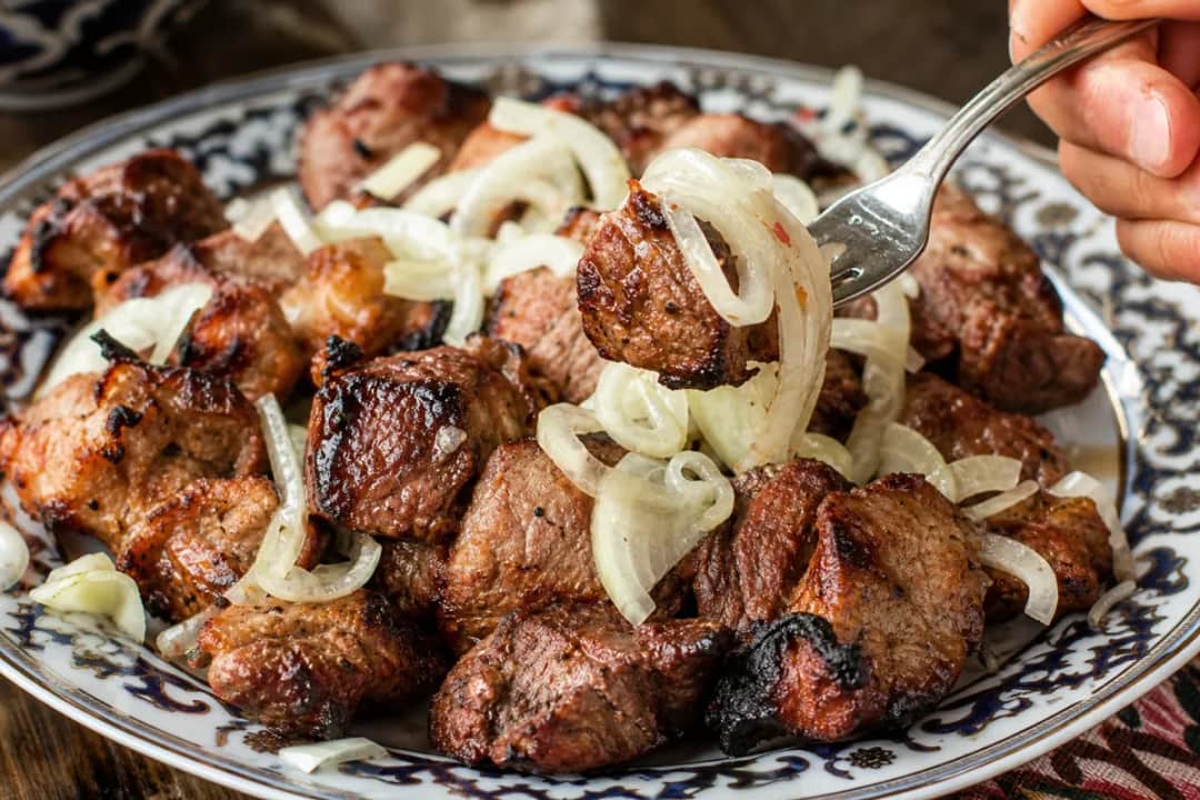 Grilled beef and lamb skewers garnished with marinated onions and herbs on a plate.